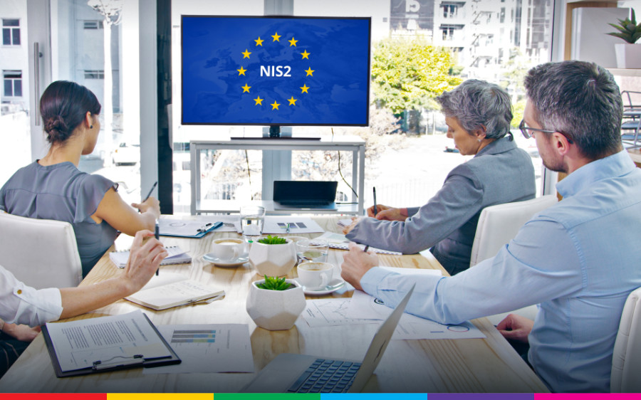 Groep werknemers zit in kantoor aan tafel en kijkt naar een scherm met daarop ‘NIS2’ tegen Europese vlag