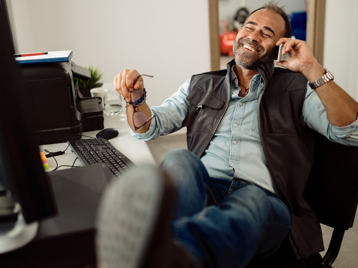 monteur zit met benen over elkaar lachend te bellen aan bureau