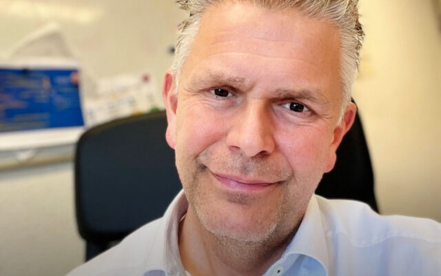 Close up van een glimlachende man met grijs haar en lichtblauwe bloes