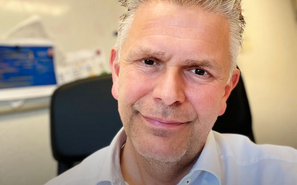 Close up van een glimlachende man met grijs haar en lichtblauwe bloes