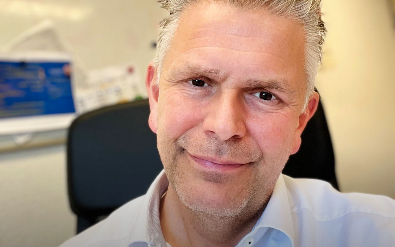 Close up van een glimlachende man met grijs haar en lichtblauwe bloes