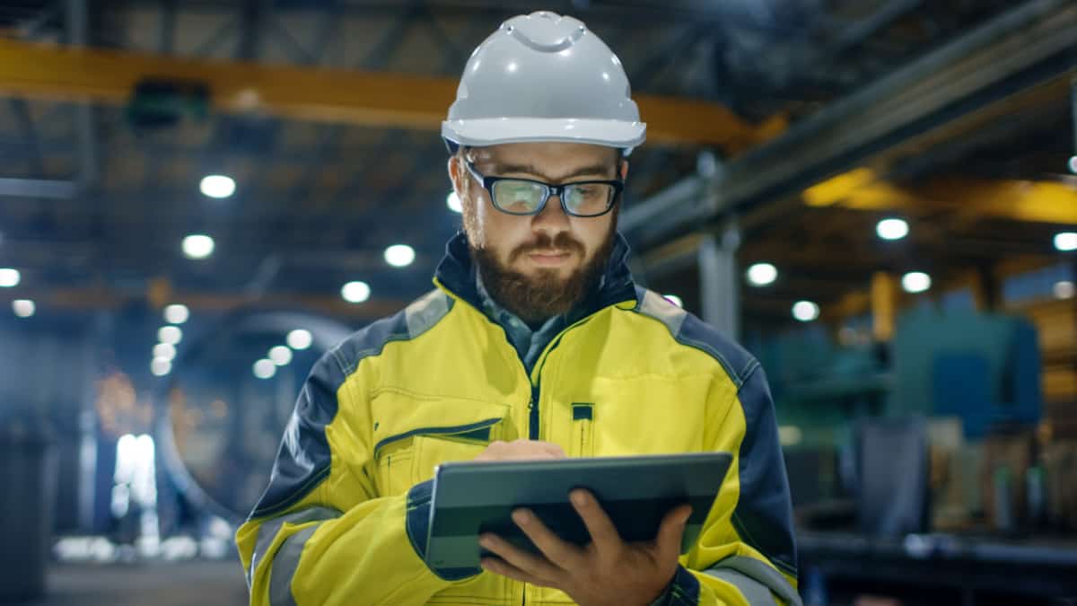 Ingenieur in werkkleding en met valhelm in werkplaats kijkt op tablet